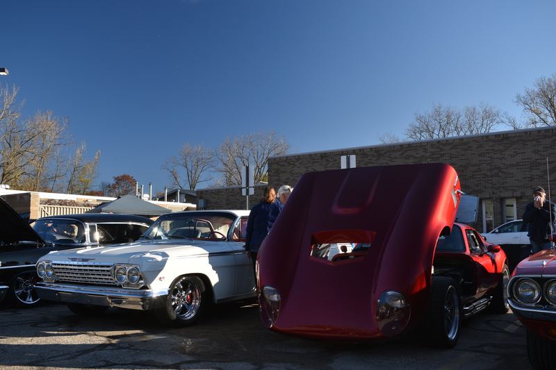 A red mid-engine show car with its rear clam open next to a white classic Impala.