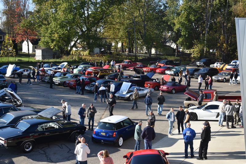 A crowd moving through the lot between parked cars, with a blue Mini in the middle.