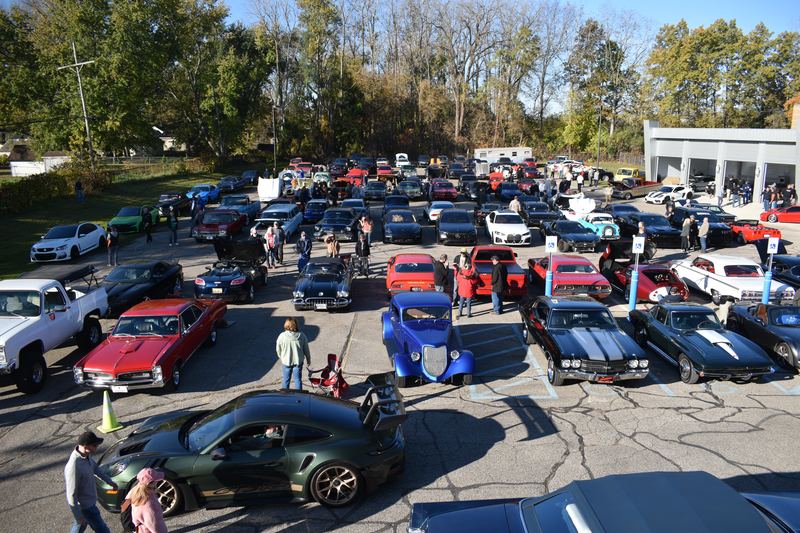 Visitors walking between rows of muscle cars, hot rods and sports cars in the lot.