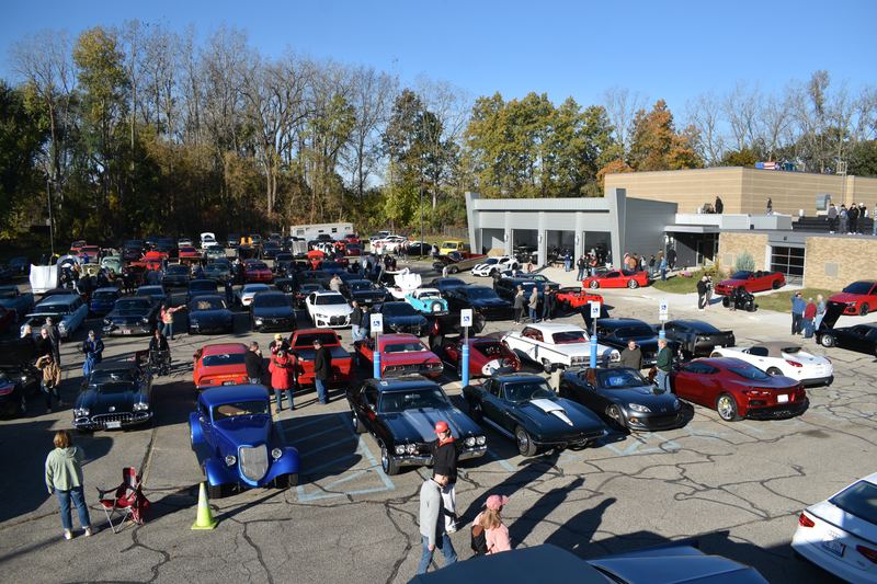 A blue hot rod and a row of striped muscle cars in the crowded lot.