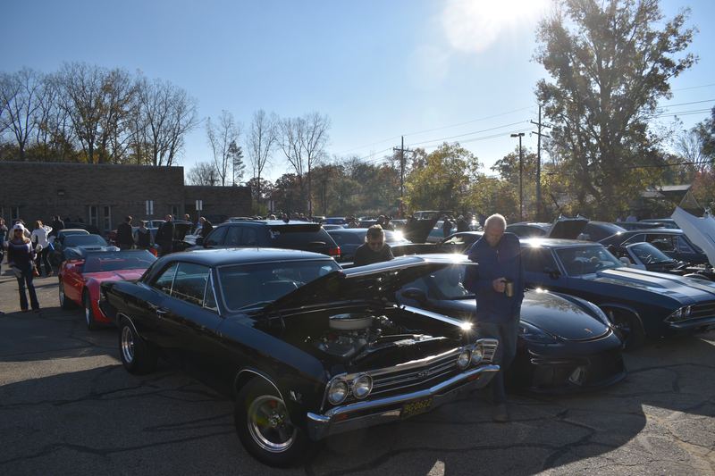 A black classic Chevelle with its hood open and its owner beside it.