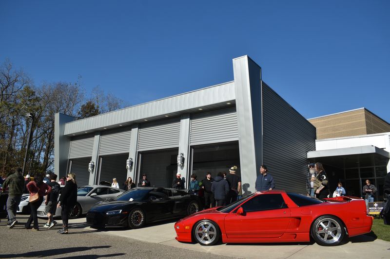 A red Acura NSX and an Audi R8 in front of the garage doors with visitors around them.